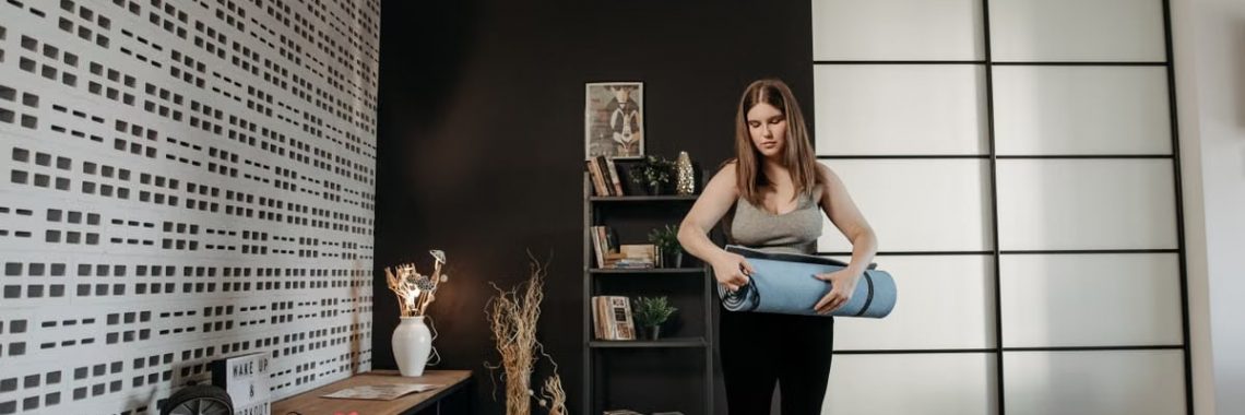 Plus size woman rolling a yoga mat in a stylish indoor setting with modern decor.