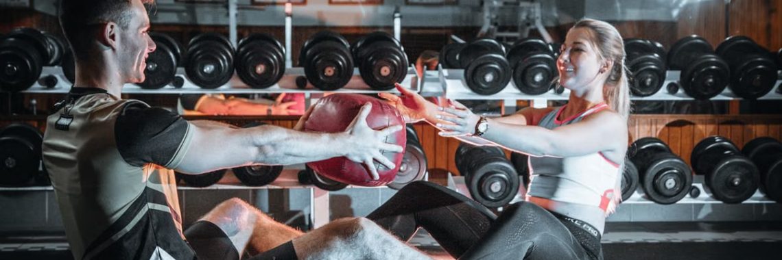 A couple engaged in a fitness session using a medicine ball in a gym environment.