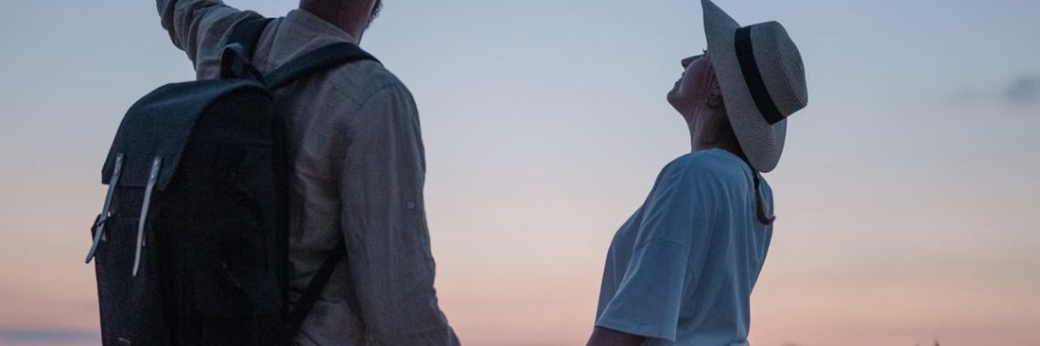 Romantic couple holding hands while watching a sunset at a serene lakeside location, embracing nature.