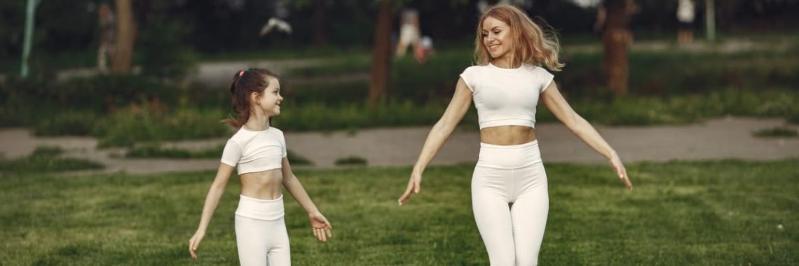 Mother and daughter bonding through outdoor exercise in activewear, featuring a joyful moment in a green park.